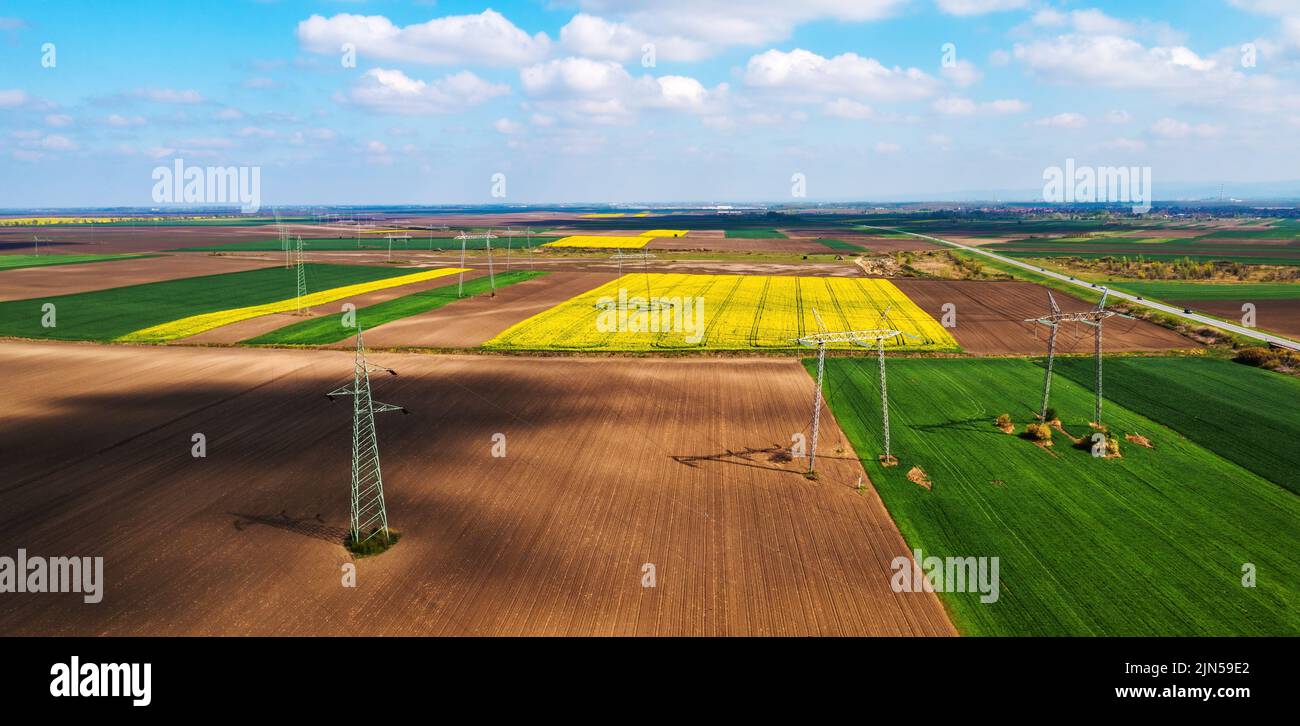 Aerial shot of transmission towers electricity pylons with power lines in cultivated agricultural field, drone pov high angle view Stock Photo