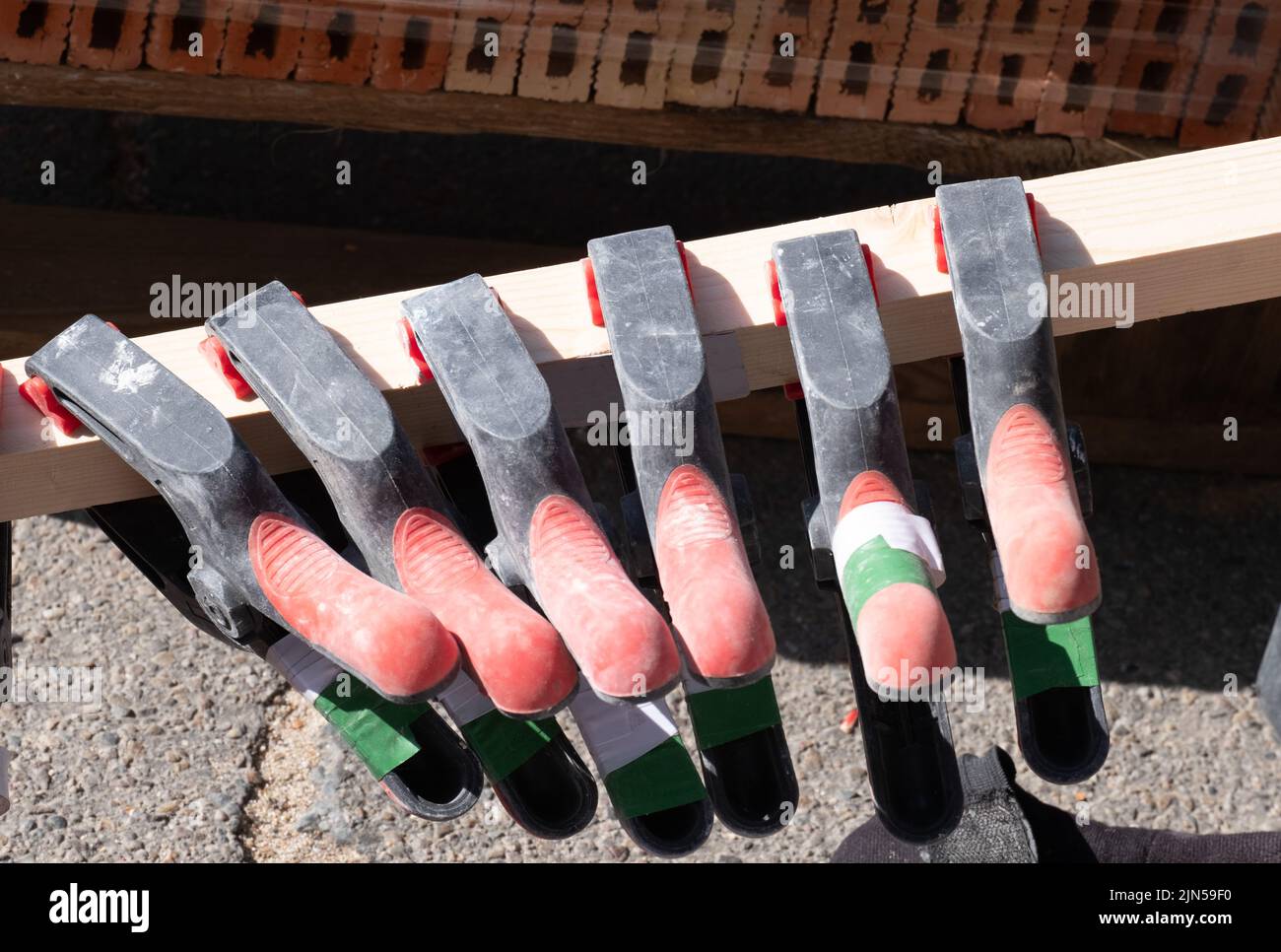 Several clamps hanging from a piece of wood await their turn to be used in the structure of a new masonry construction Stock Photo