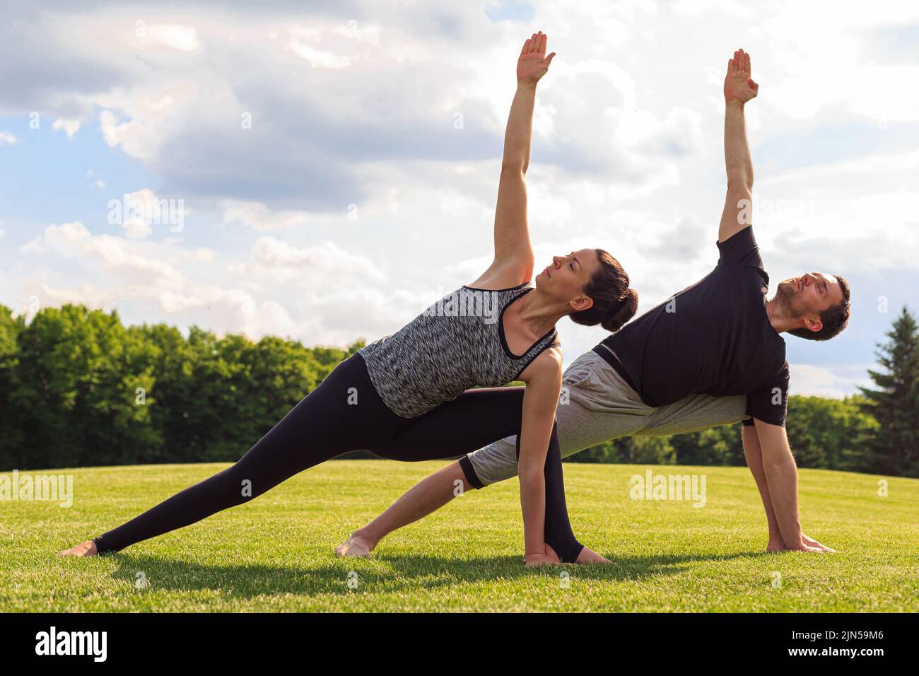 Young healthy man and woman doing yoga in the sunny summer park. Fitness and healthy lifestyle Stock Photo