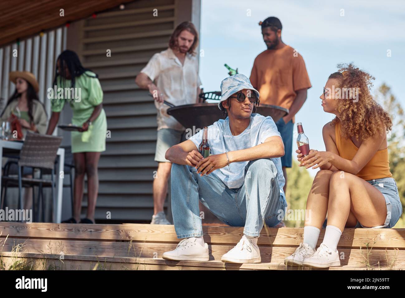 Diverse group of young people enjoying drinks during outdoor dinner in Summer cabin, focus on couple in foreground Stock Photo
