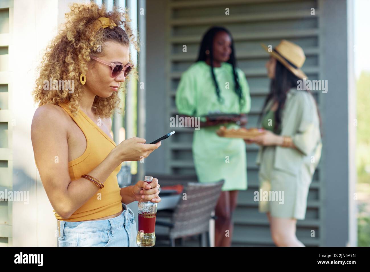Side view portrait of young woman holding smartphone during barbeque party outdoors in Summer, copy space Stock Photo