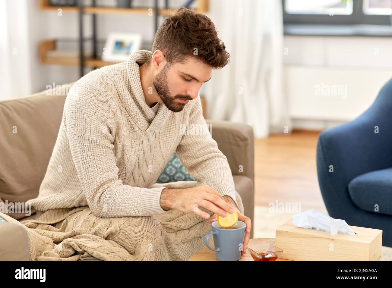 sick young man in blanket drinking hot tea at home Stock Photo