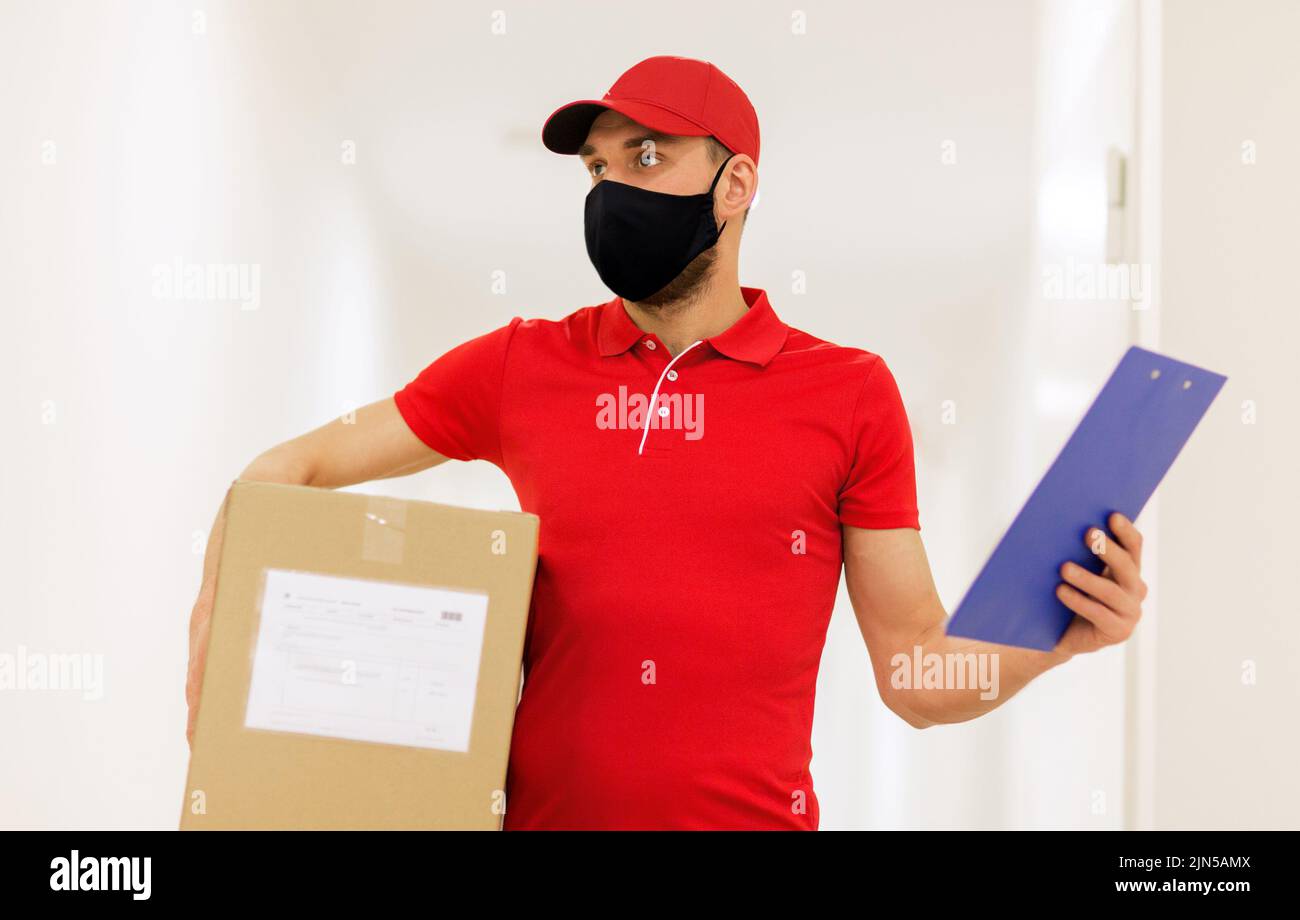 delivery man in mask with box and clipboard Stock Photo