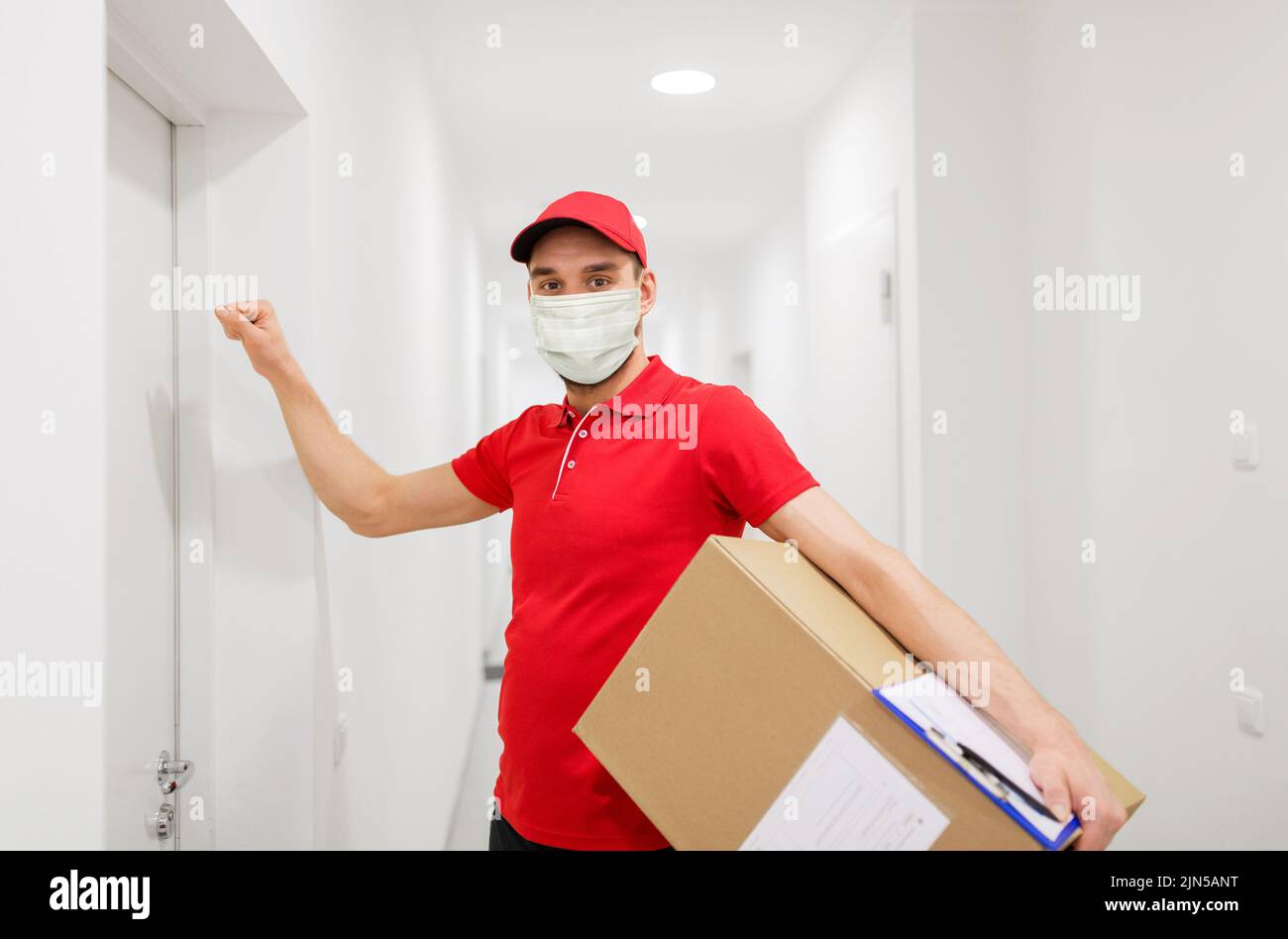 delivery man in mask with parcel knocking on door Stock Photo