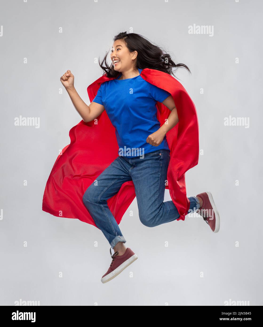 happy asian woman in red superhero cape jumping Stock Photo