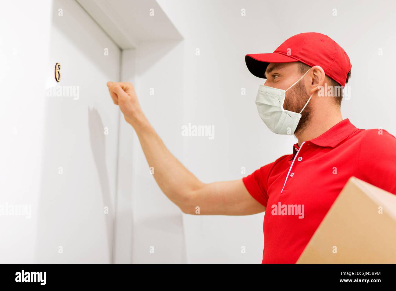 delivery man in mask with parcel knocking on door Stock Photo