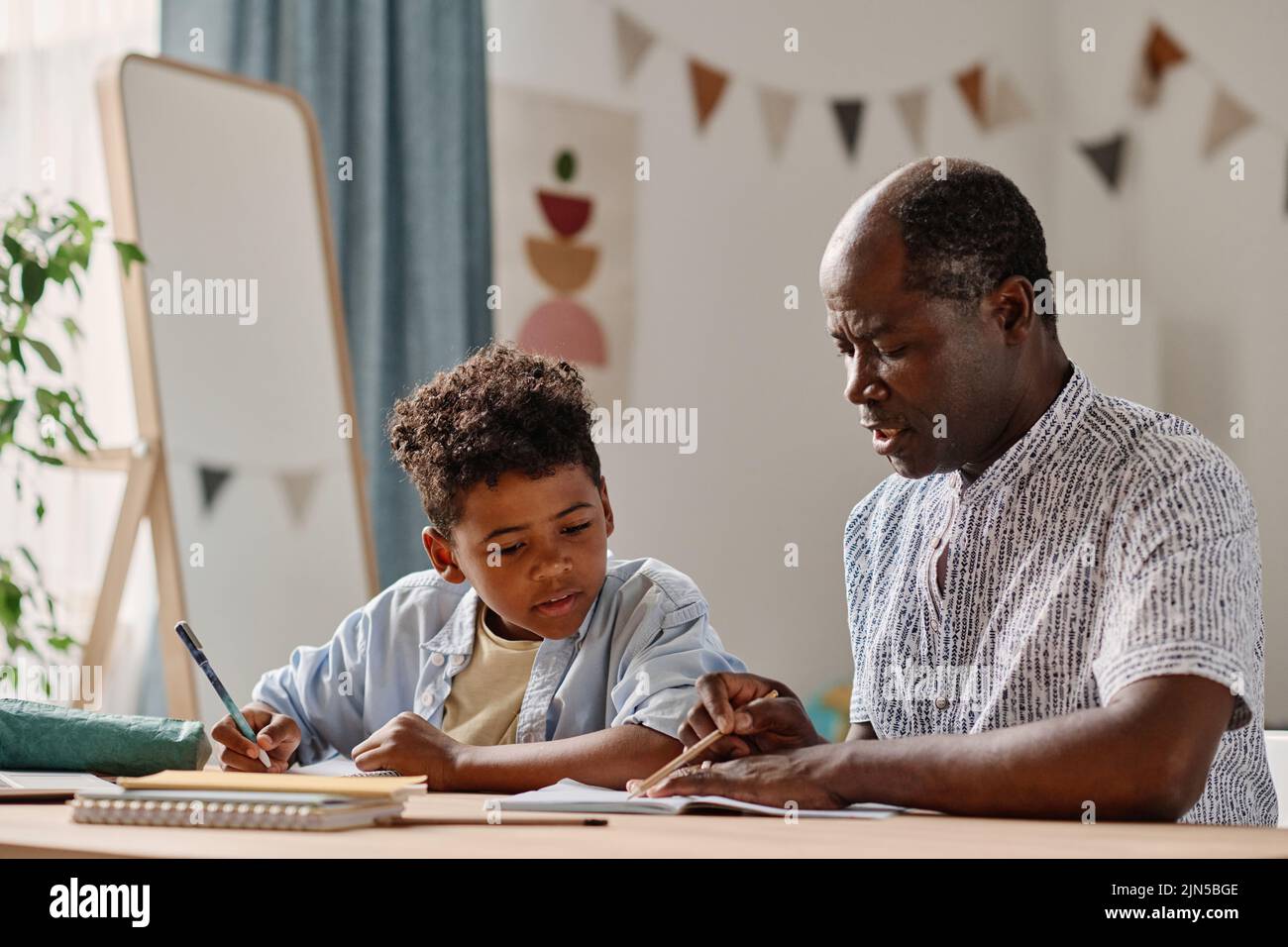 African teacher explaining the new material to little boy at table in ...