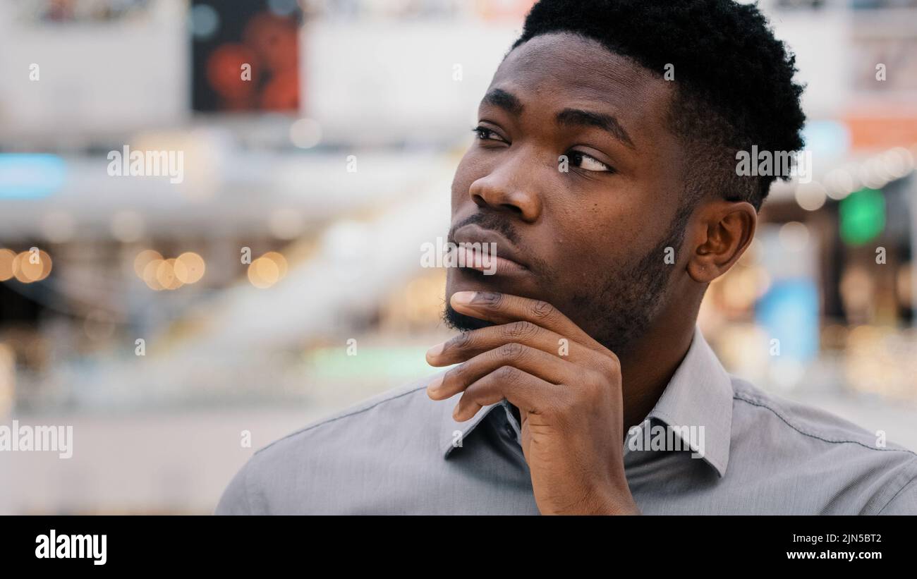 Close-up puzzled concentrated pensive serious african american young man looking away keeps hand on chin thinks solves problem comes up with new Stock Photo