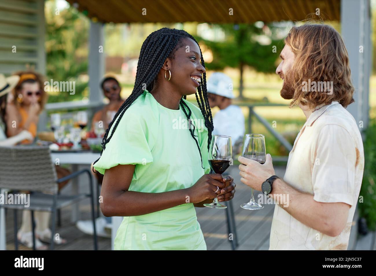 Side view portrait of young couple chatting and enjoying glass of wine during outdoor party with friends in Summer, copy space Stock Photo