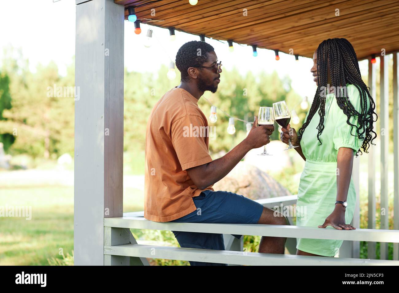 Side view portrait of black young couple chatting and enjoying glass of wine at terrace during outdoor party in Summer, copy space Stock Photo