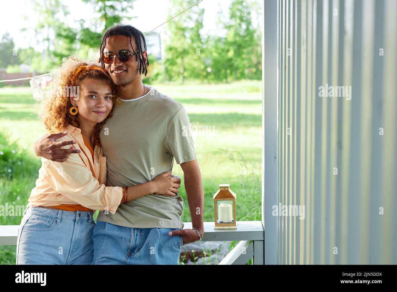 Waist up portrait of loving black couple embracing and looking at camera at outdoor terrace in Summer, copy space Stock Photo