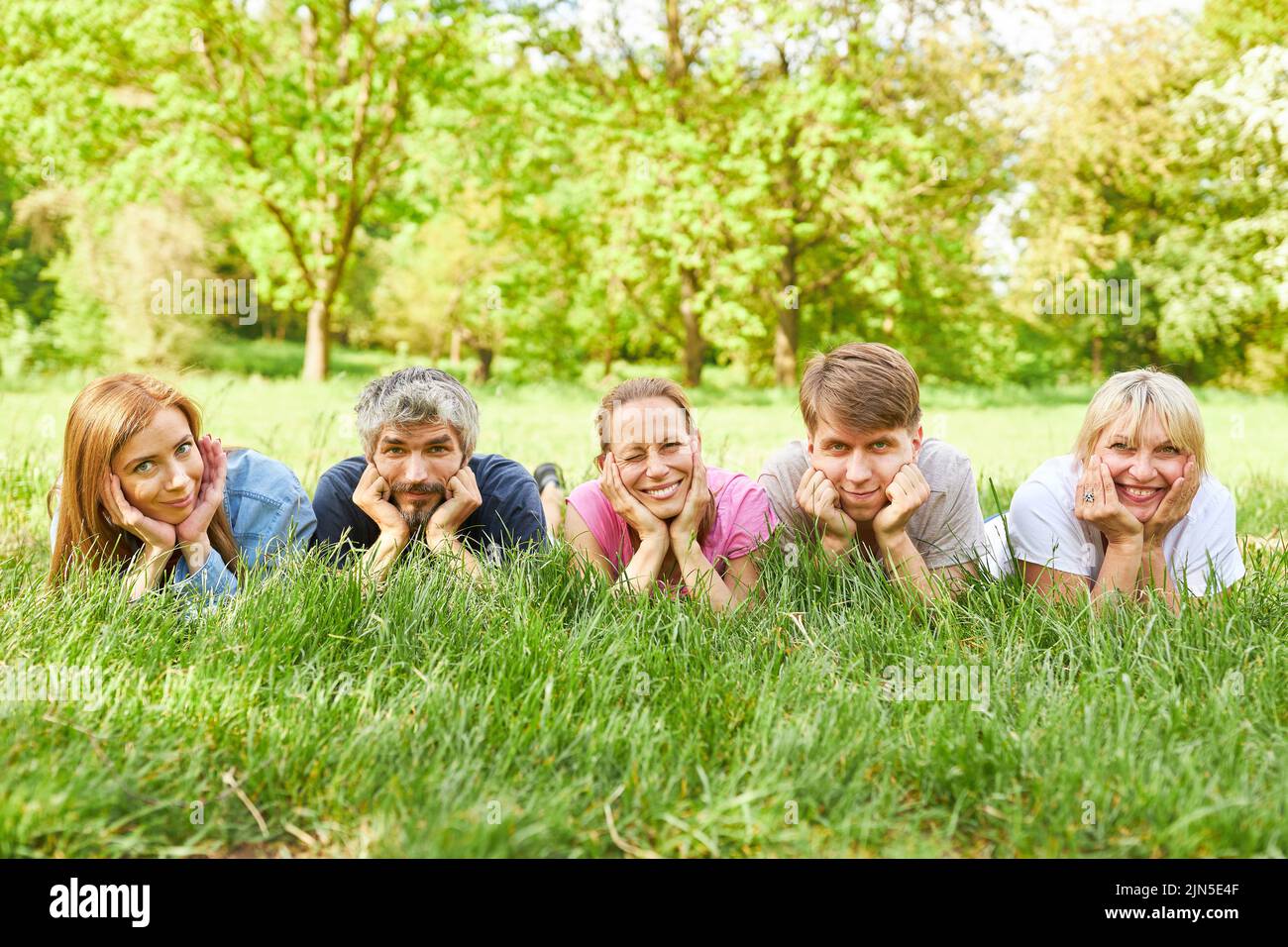 Family or friends take a break in a meadow in summer and lie relaxed in the grass Stock Photo