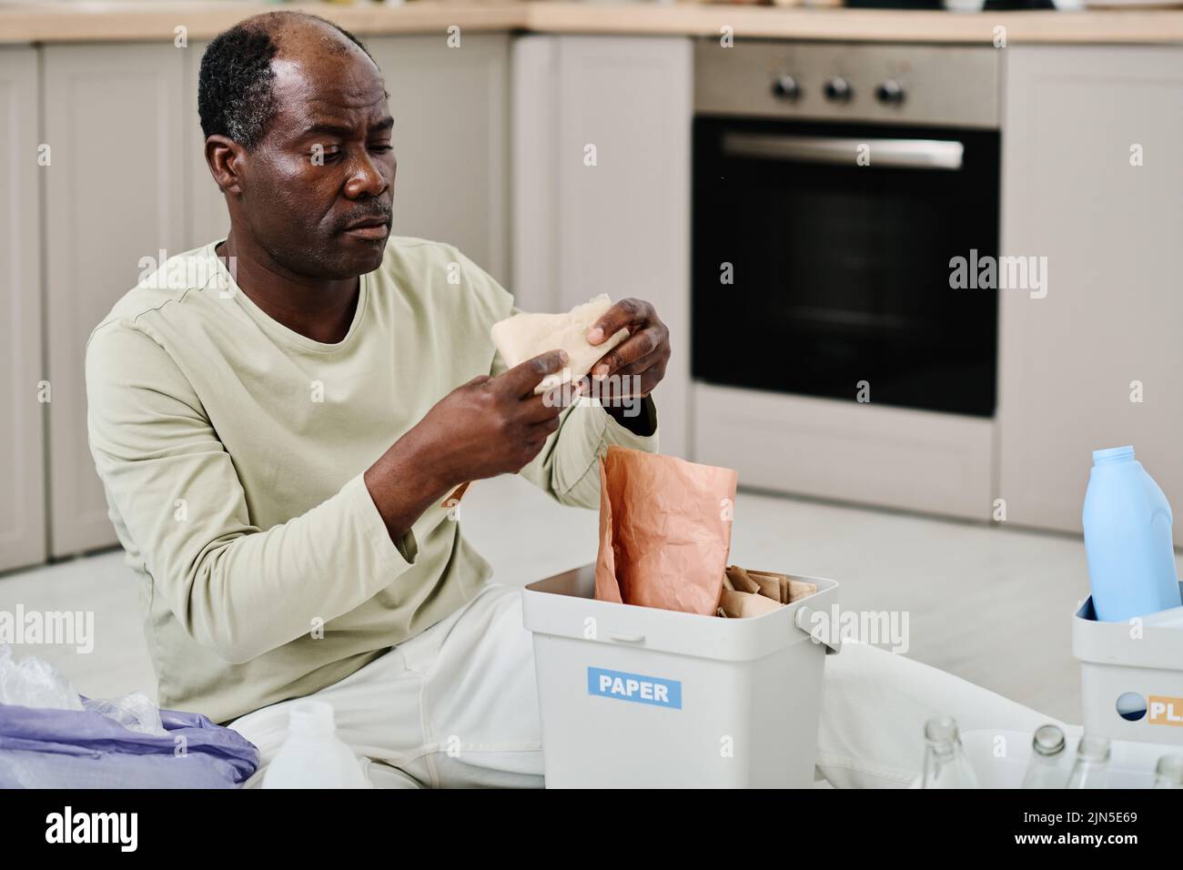 African man putting papers in container, he separating garbage in the kitchen for recycling Stock Photo