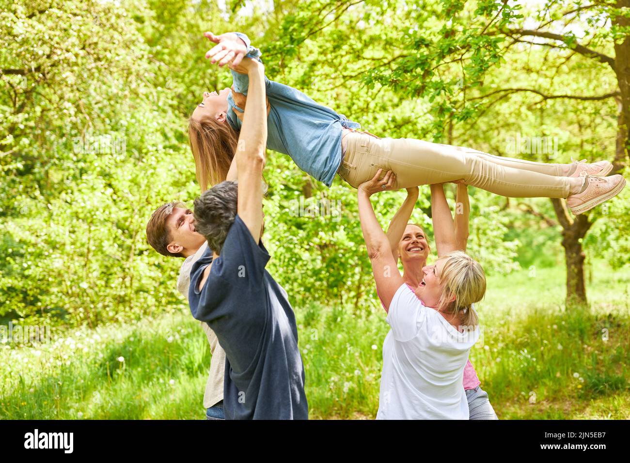 Athletic team of young people lift a woman up in the air together as a team building exercise Stock Photo