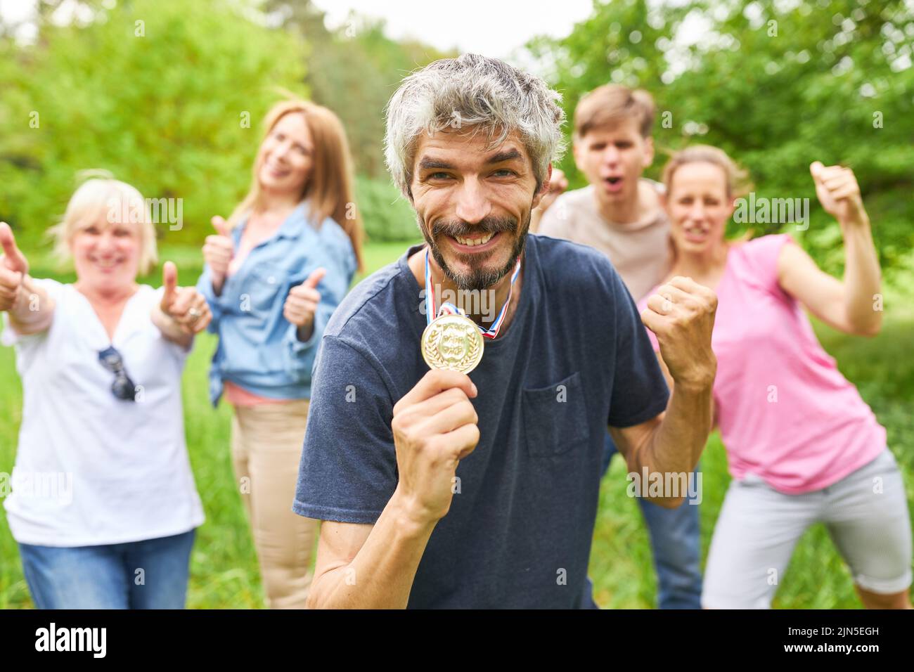 Successful man shows his medal and celebrates with his team after a win Stock Photo