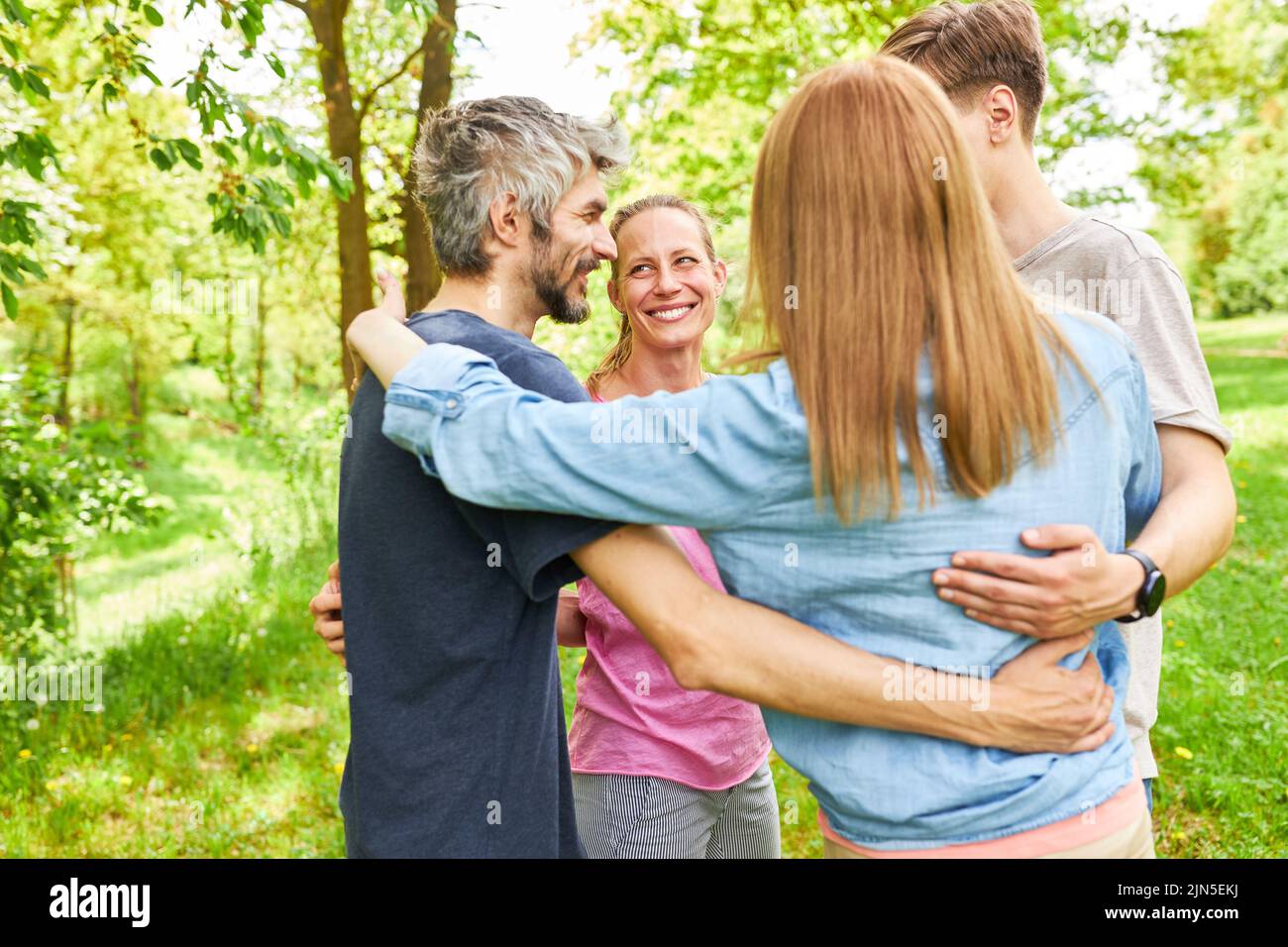 Young people standing in circle and hugging as friends on nature in park in summer Stock Photo