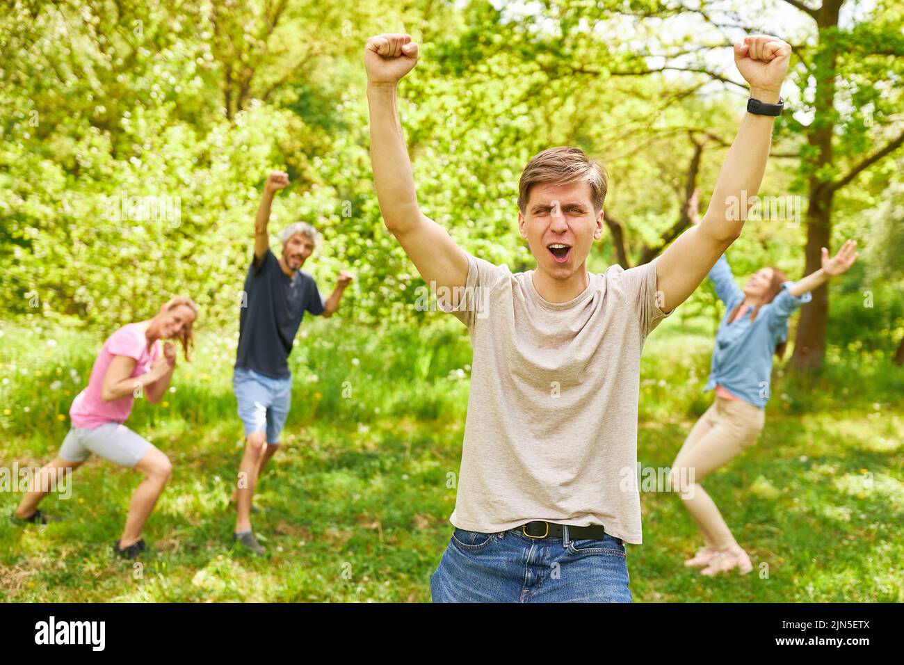 Happy young man cheering with clenched fists with winning team in background Stock Photo