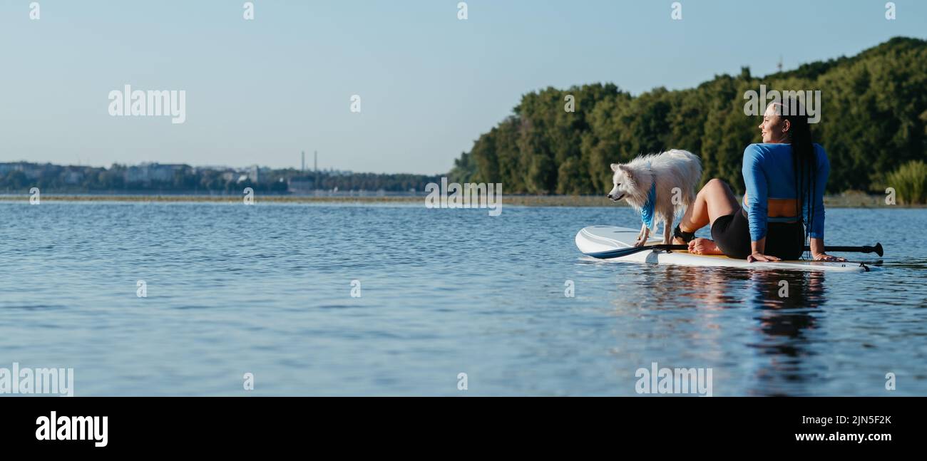 Young Woman Relaxing on the City Lake While Sitting on the Sup Board with Her Dog Japanese Spitz Stock Photo