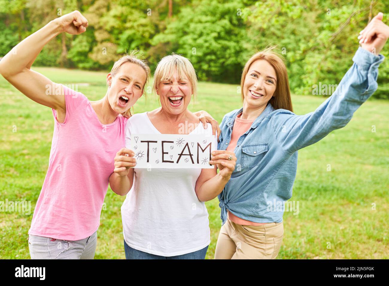 Three women cheering as winners with team sign in hands as concept for girl power Stock Photo