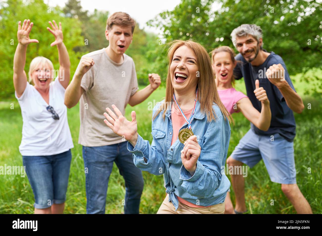 Cheering team and young woman with winner medal after a success at team event Stock Photo