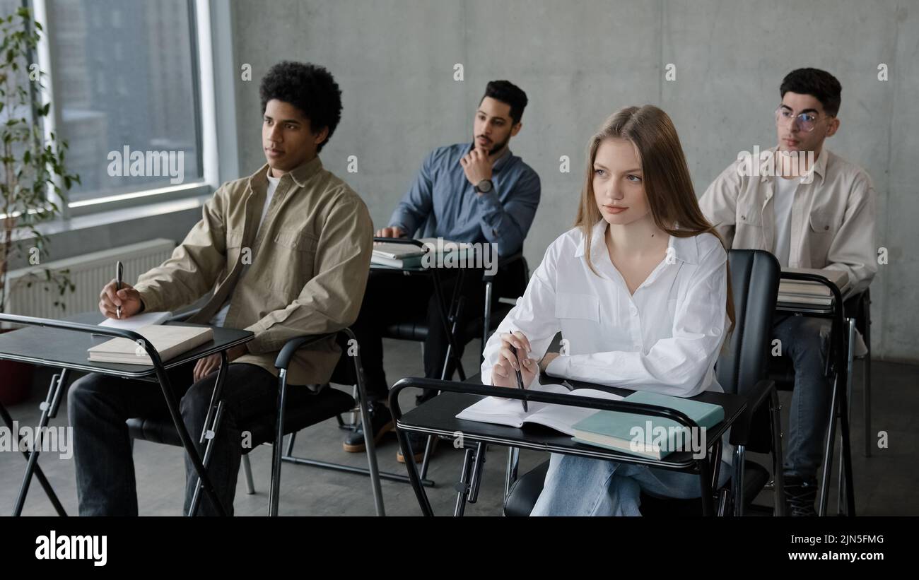 Students sit at desk in classroom attentive listen lecture at seminar write notes prepare for exam business audience at conference group young people Stock Photo