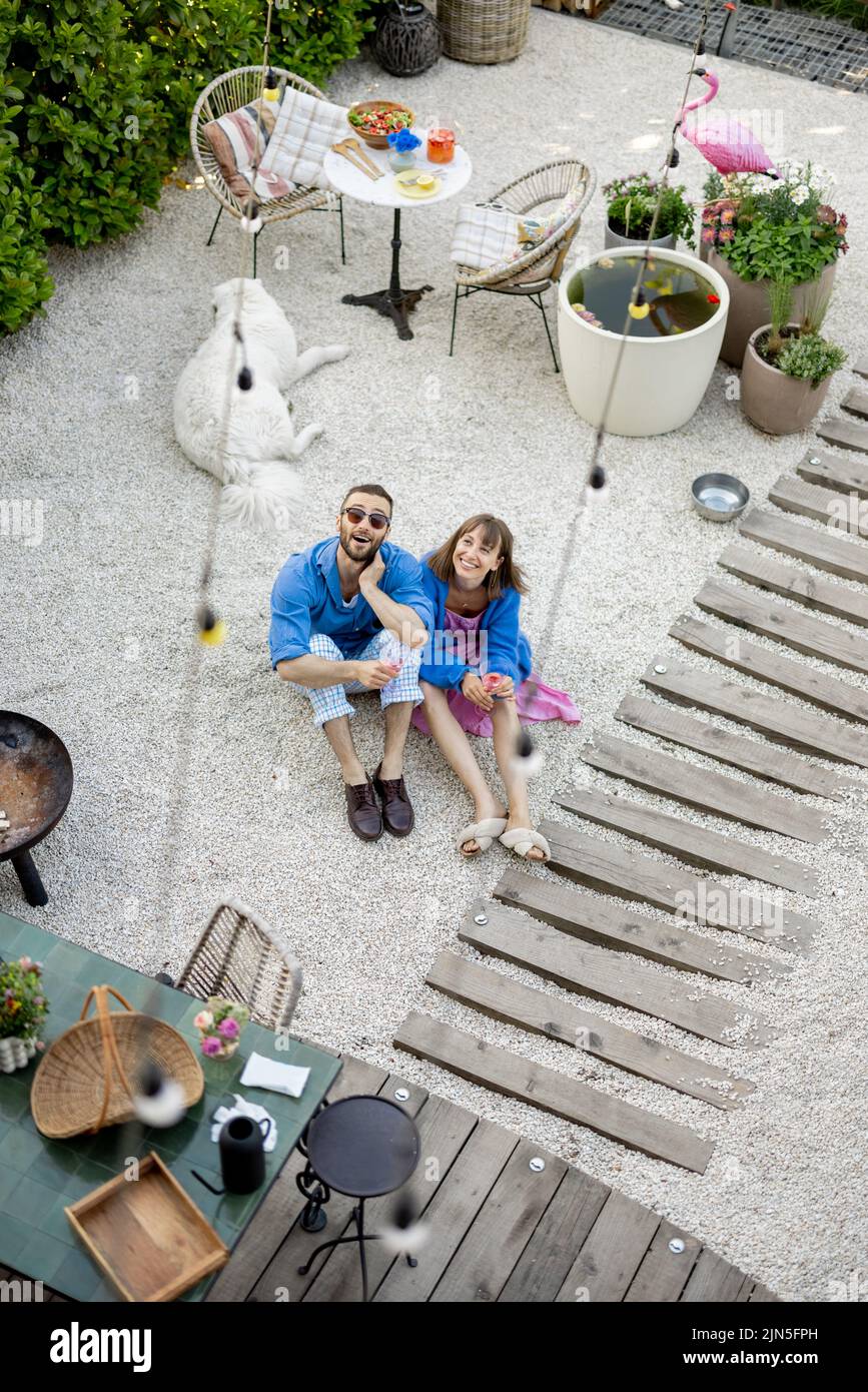 Young stylish couple sit together at their beautiful backyard, wide view from above. Spending summer time at cozy garden Stock Photo