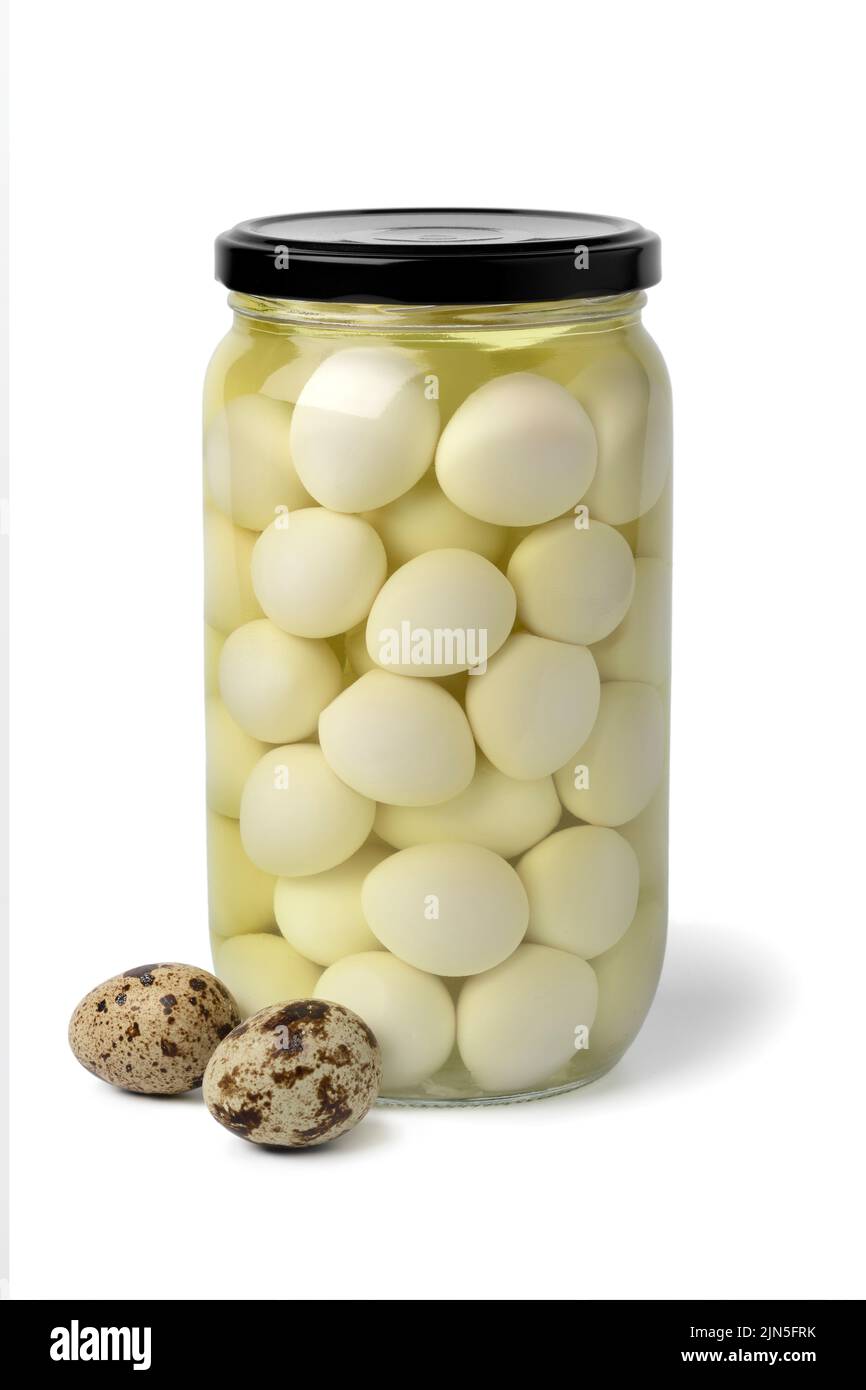 Glass jar with preserved cooked Quail eggs in water close up isolated on white background with fresh raw eggs in front Stock Photo