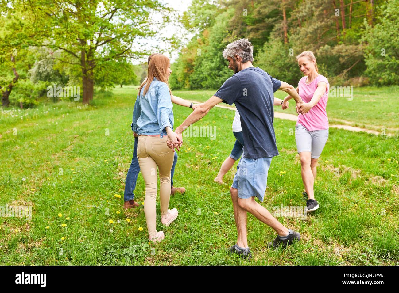 Young people doing exercise in team building workshop running in a circle on a meadow in the park Stock Photo