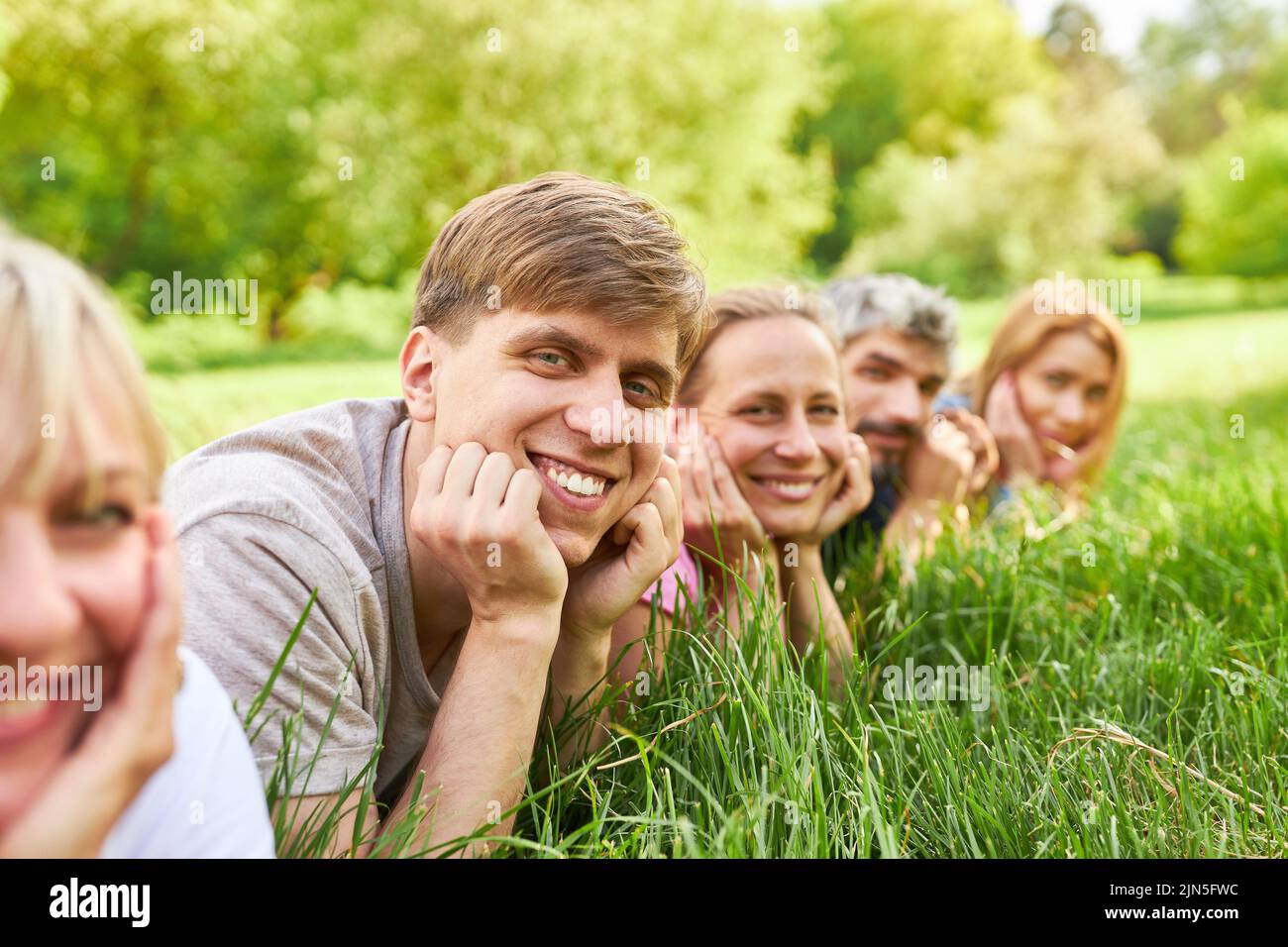 Smiling young man lying relaxed on a meadow with his friends Stock Photo
