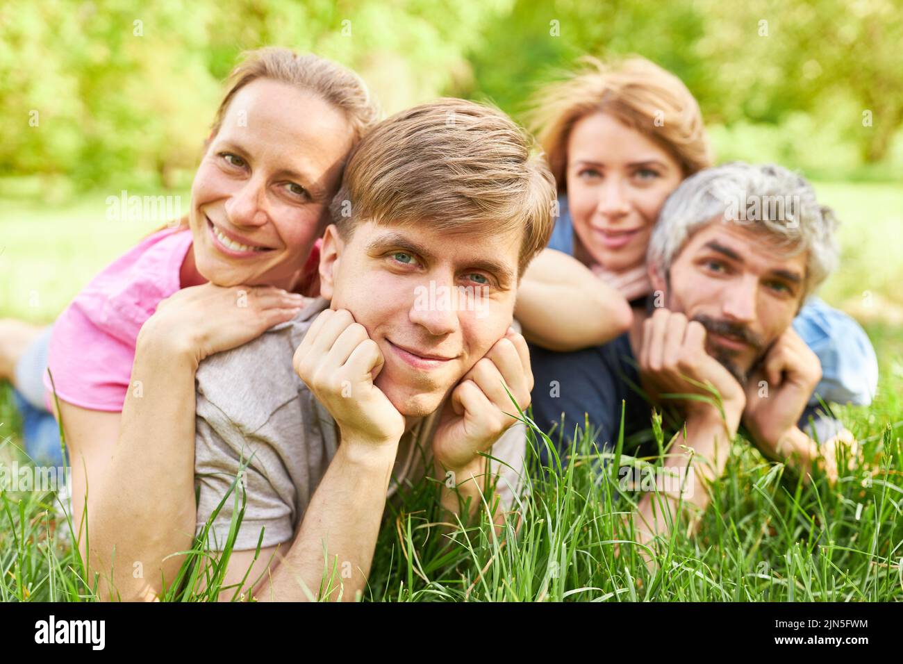 Two happy young couples lie in the grass on a meadow in summer and relax Stock Photo
