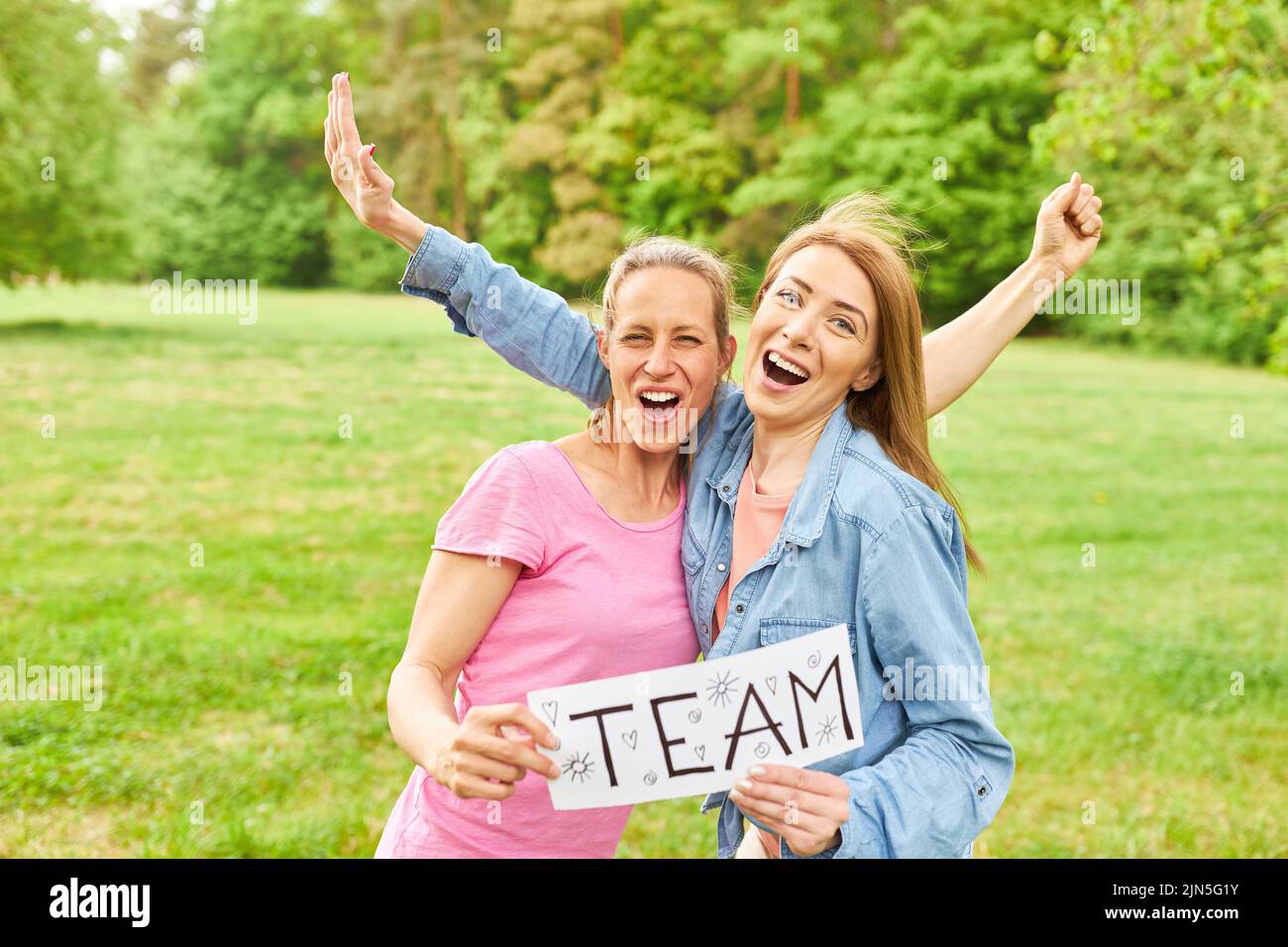 Two cheering women as a successful team hold sign with team as the inscription Stock Photo