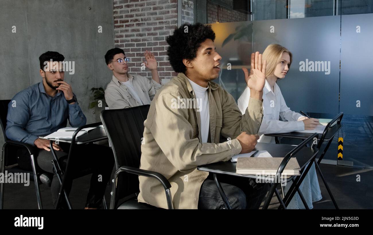 Diverse people sit in classroom at desk actively study science classmates students listen lecture seminar in college studying at school raise hands Stock Photo