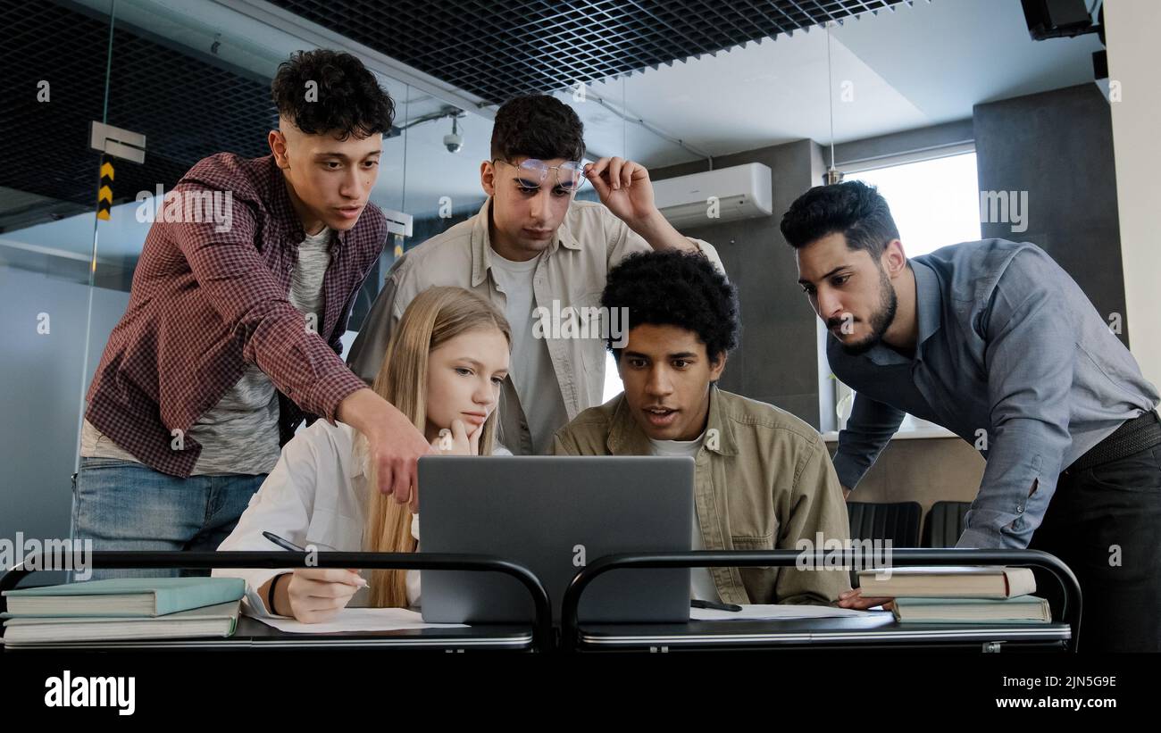 Young corporate employees sitting in office looking at laptop screen reading good news excited happy team diverse people celebrating victory win Stock Photo