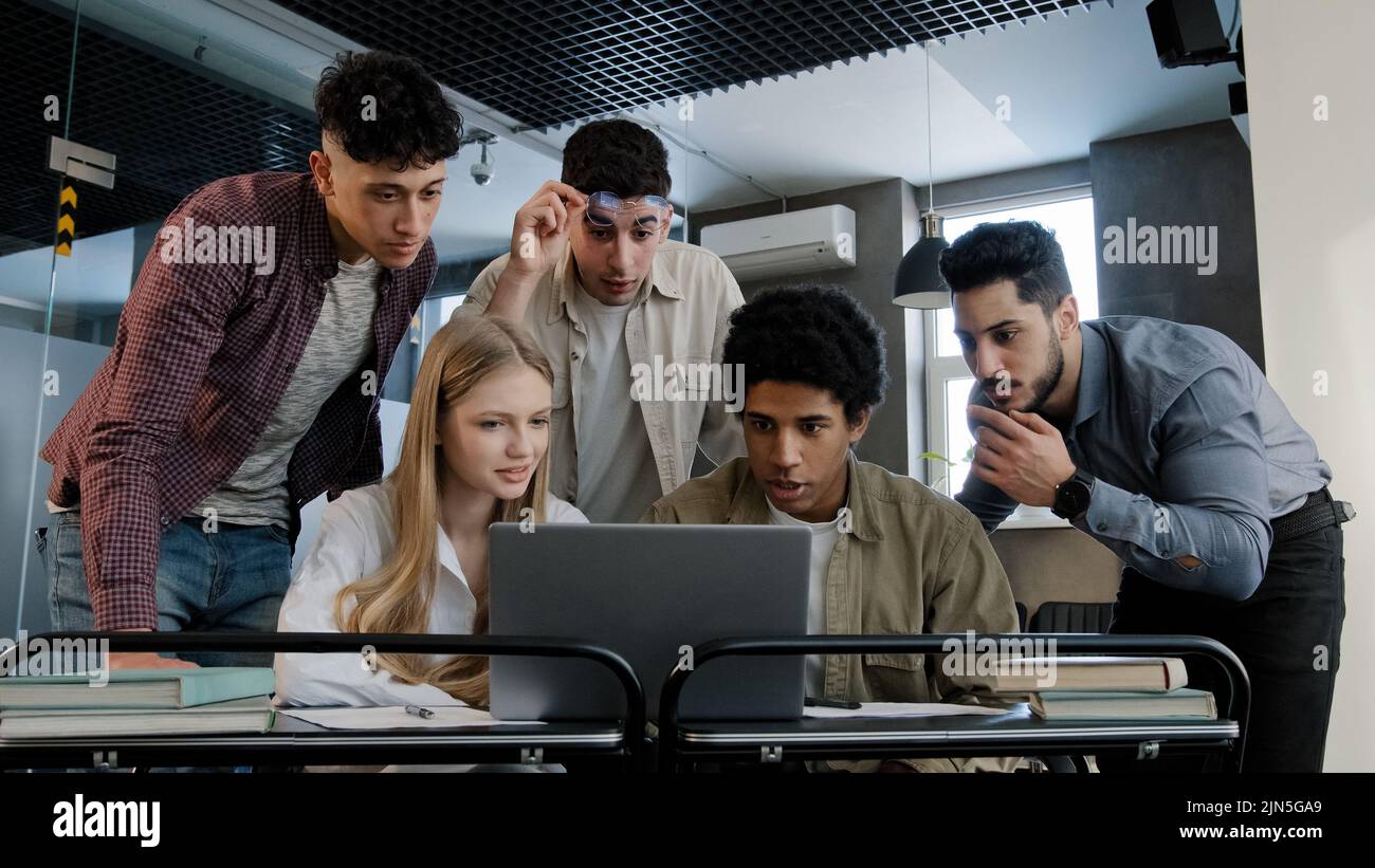 Focused diverse team corporate employees colleagues in office looking at laptop screen reading good news happy excited group workers celebrating Stock Photo