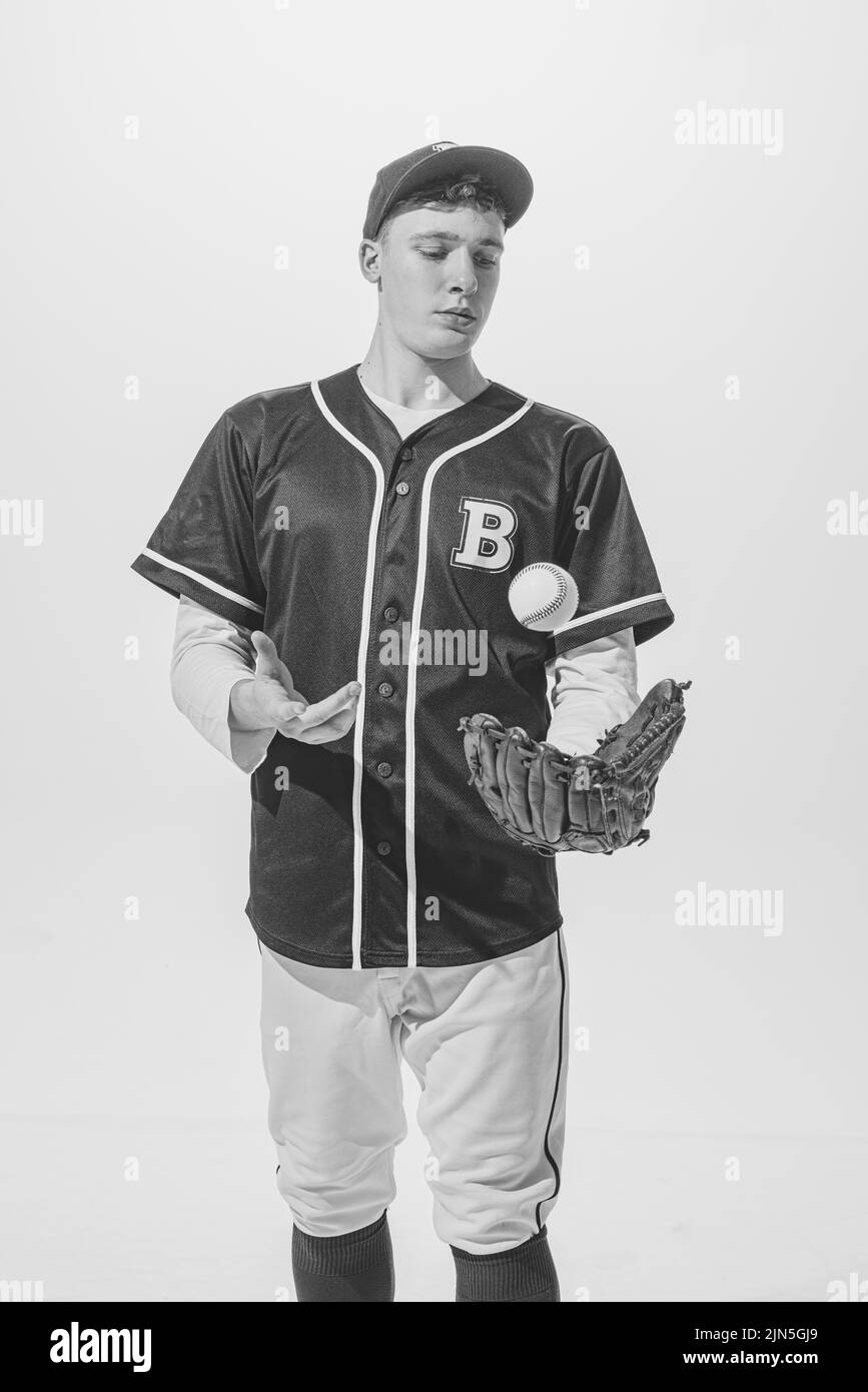 Portrait of young man, baseball player in uniform posing with ball and glove. Black and white photography Stock Photo
