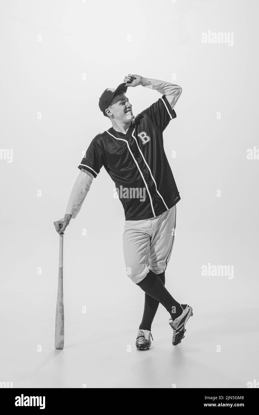 Full-length portrait of young smiling man, baseball player in uniform, leaning on bat, posing. Black and white photography Stock Photo
