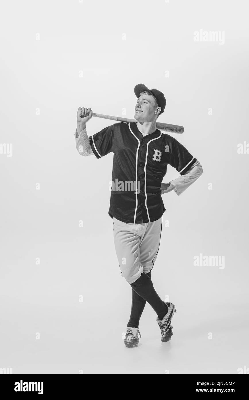 Portrait of delightful young man, baseball player, batter in uniform posing with bat. Black and white photography Stock Photo