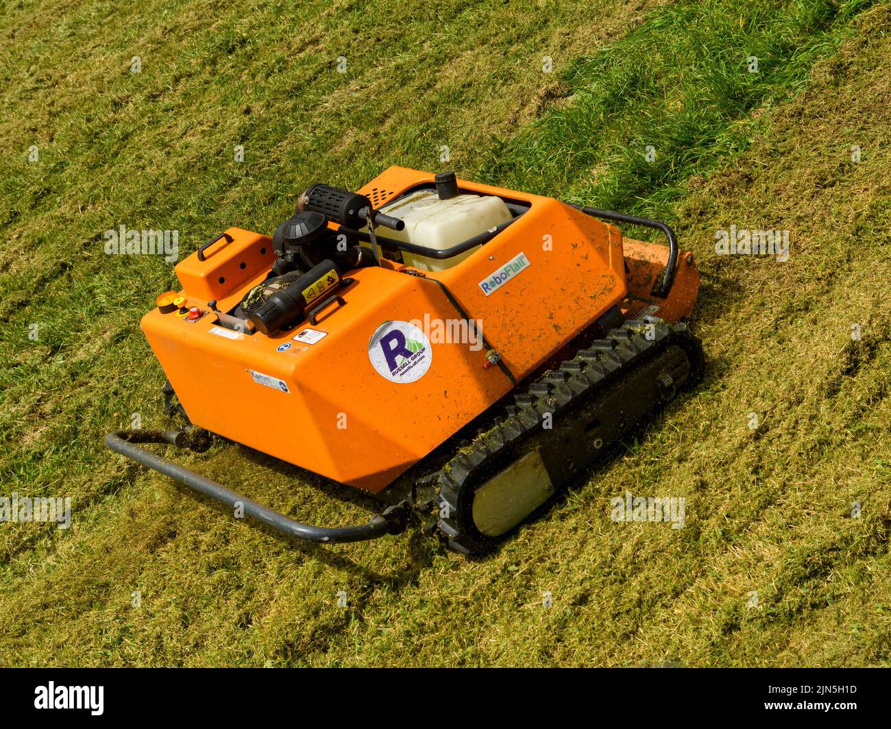 KommTek RoboFlail groundcare equipment close-up (slope & bank mowed by remote-controlled orange robotic mower) - York city wall, Yorkshire England UK. Stock Photo