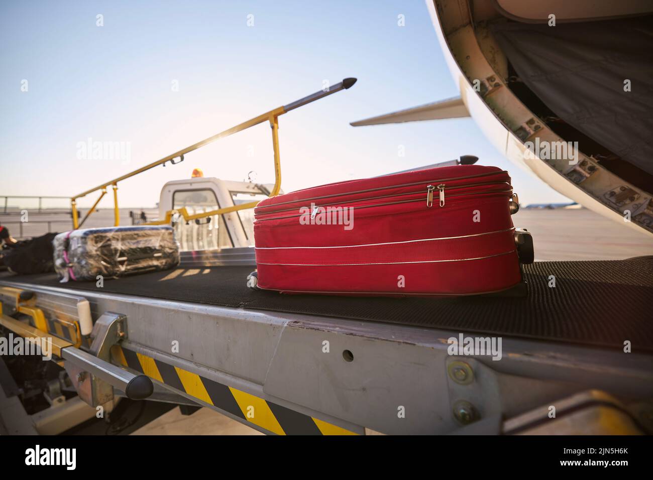 Loading of luggage to airplane. Red suitcase on conveyor belt at airport. Stock Photo