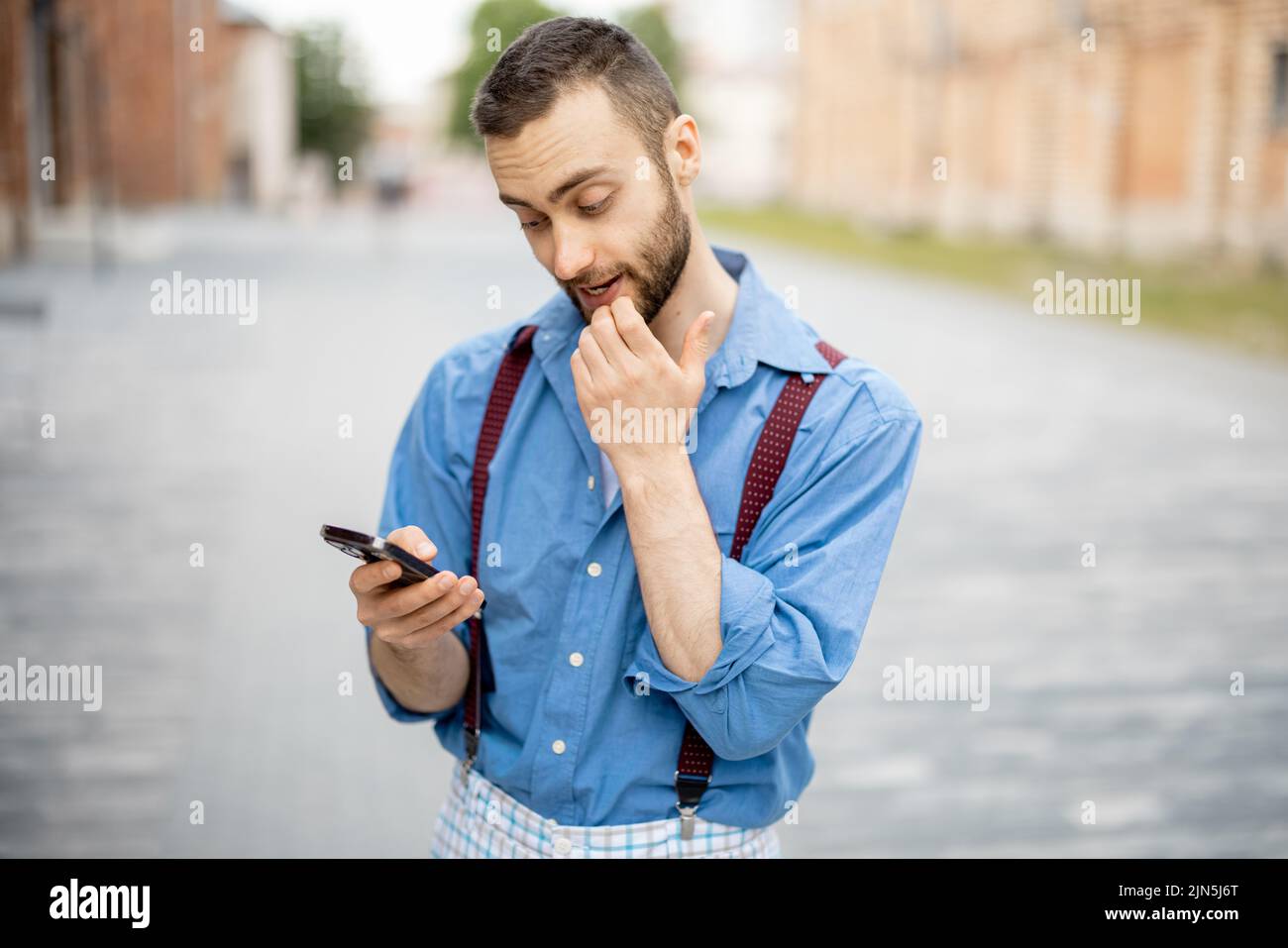 Portrait of weird businessman uses phone outdoors. Cool guy wearing blue shirt with suspenders Stock Photo