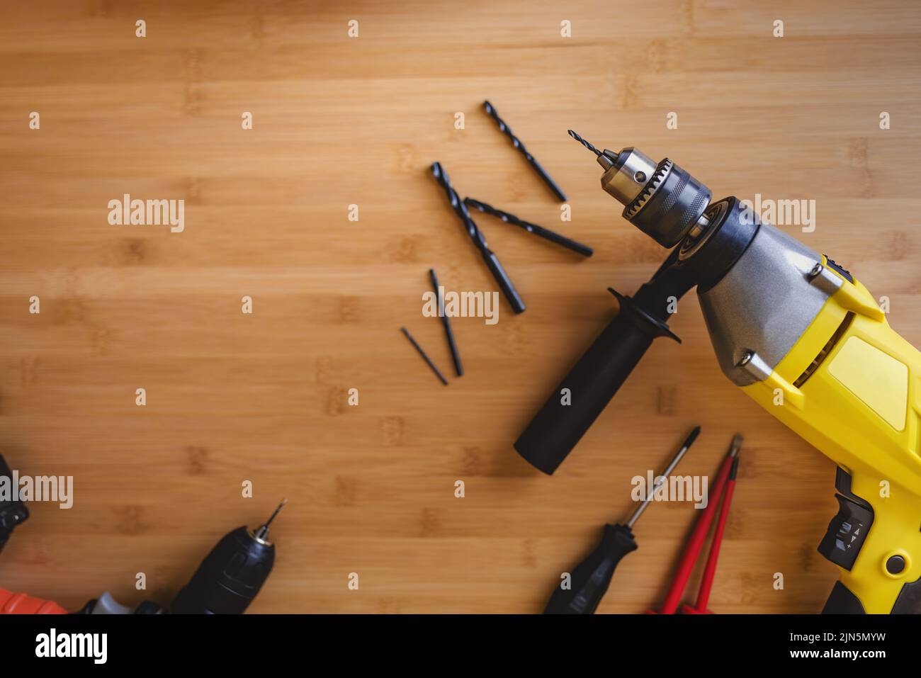 Flat lay view of drills with different drills and screwdrivers lying on a wooden table top. Stock Photo