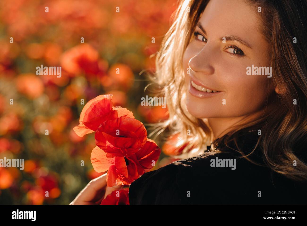 a girl in a black dress on a poppy field at sunset Stock Photo - Alamy