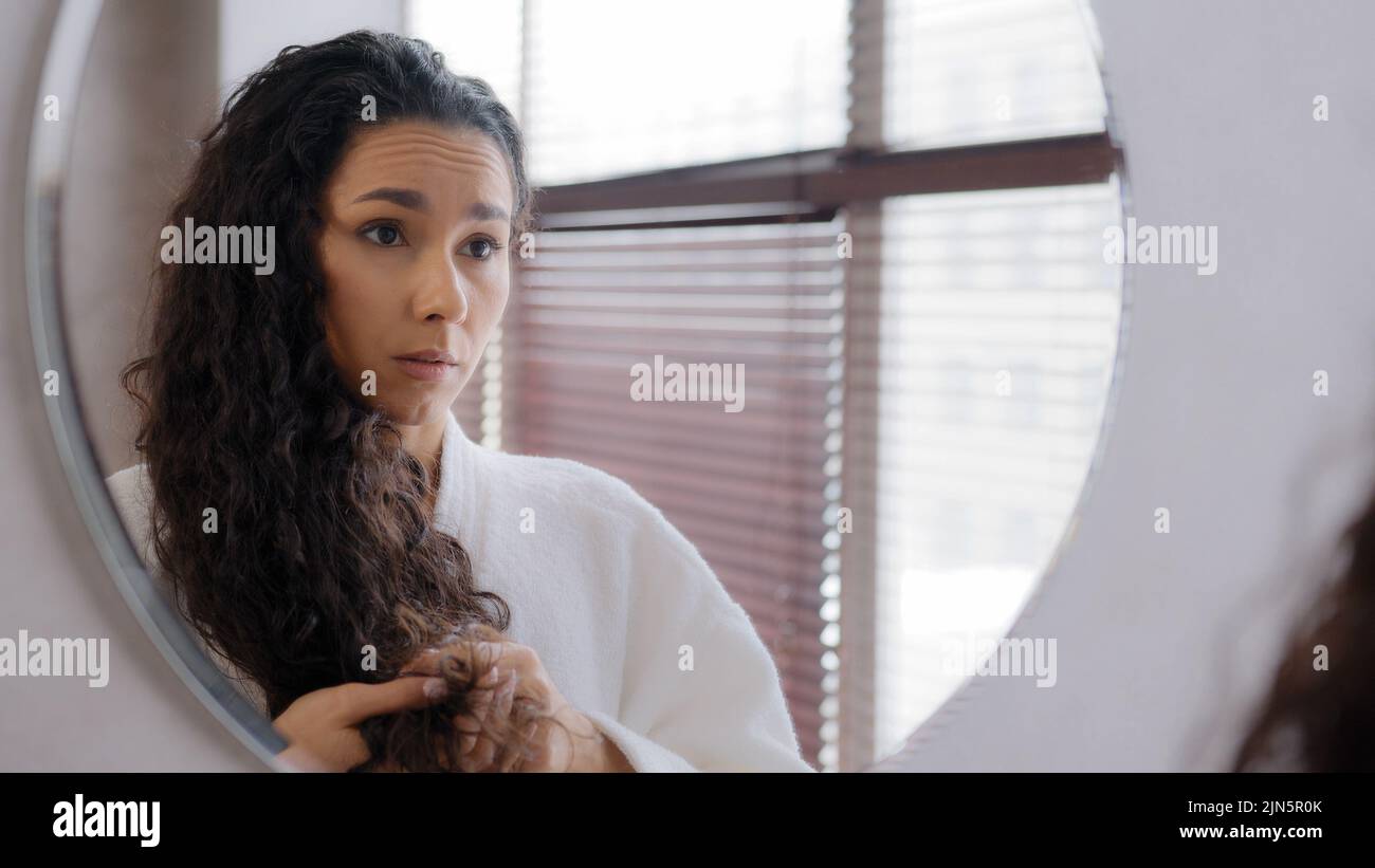 Worried upset young woman standing in bathroom in bathrobe reflected in