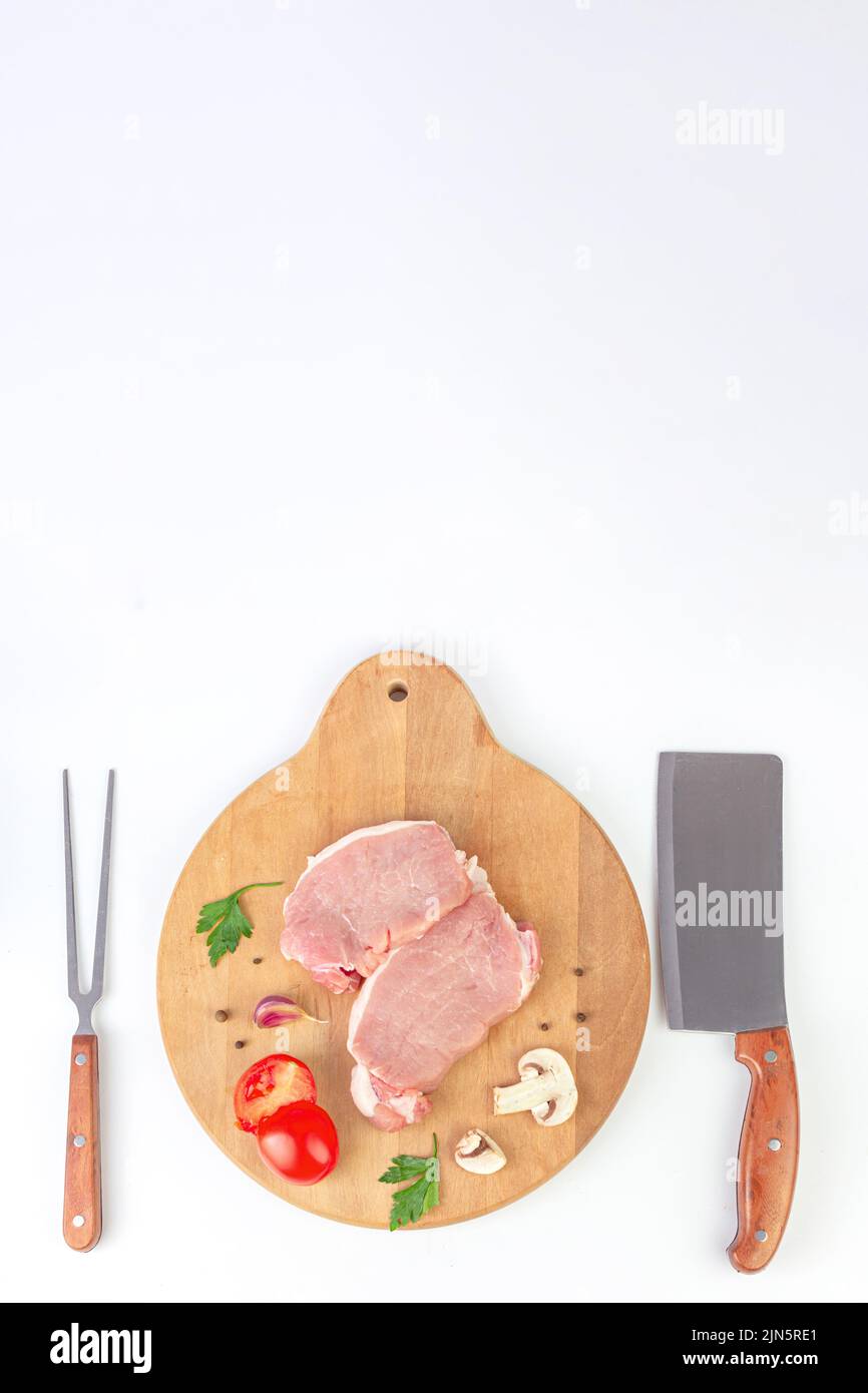 Pieces of raw beef steaks with meat fork and knife, garlic, tomato, spice, pepper, champignon Stock Photo