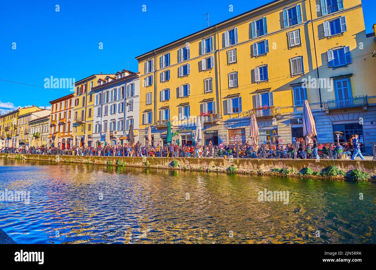 MILAN, ITALY - APRIL 9, 2022: Outdoor evening restaurants along historical houses on Naviglio Grande Canal, on April 9 in Milan, Italy Stock Photo