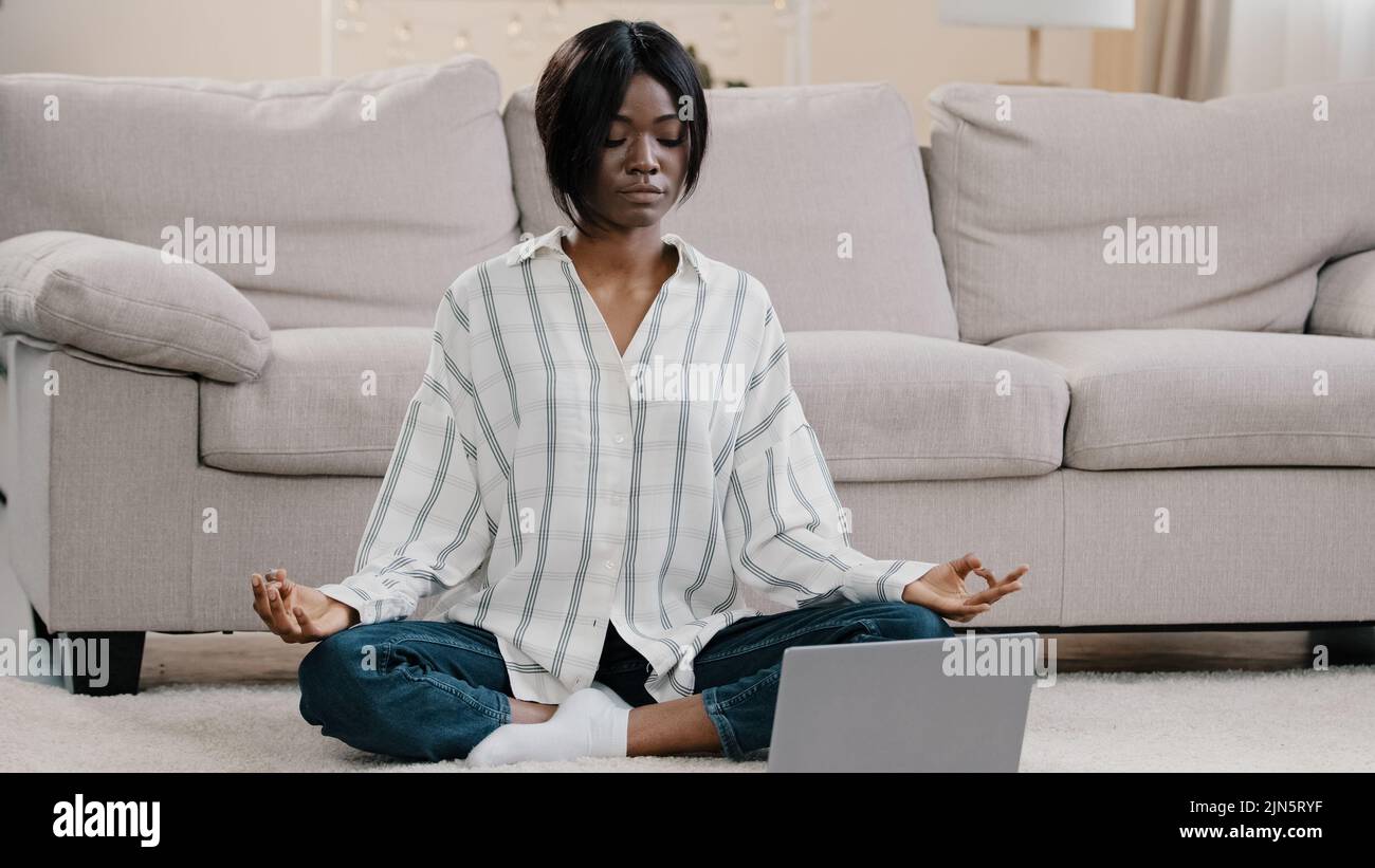 Young concentrated woman sitting in lotus position with closed eyes on floor in room attractive calm girl doing meditation improves mental health Stock Photo