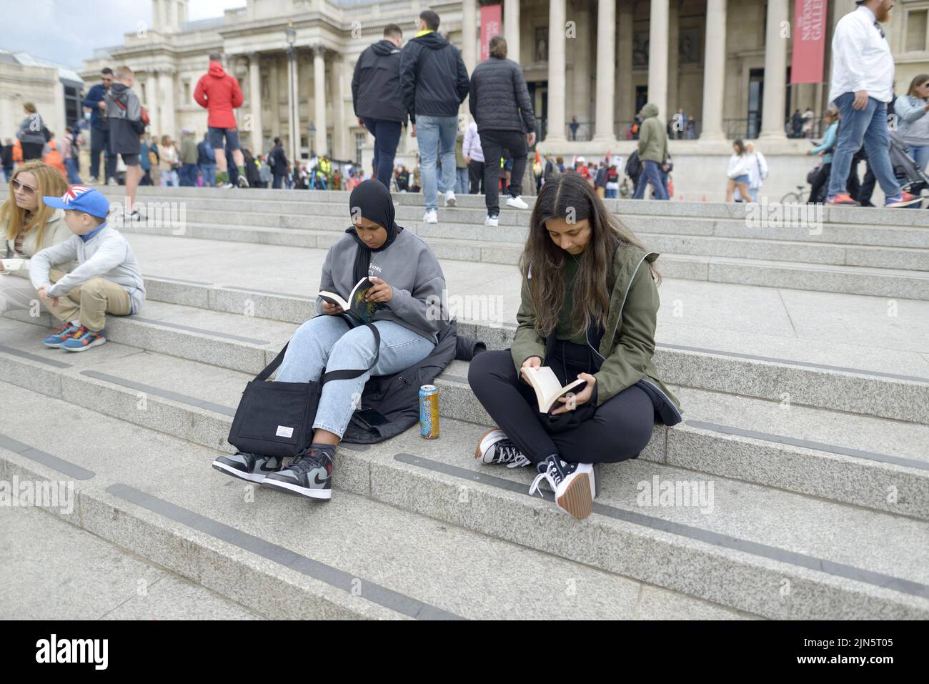 London, England, UK. Two young women reading books on the steps in Trafalgar Square Stock Photo
