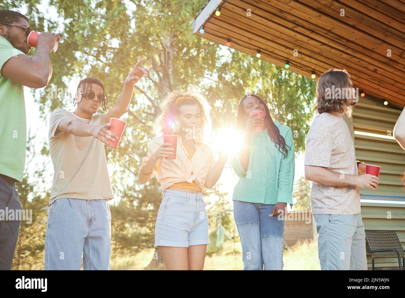 Vibrant shot of diverse group of young people dancing outdoors during Summer party with lens flare Stock Photo
