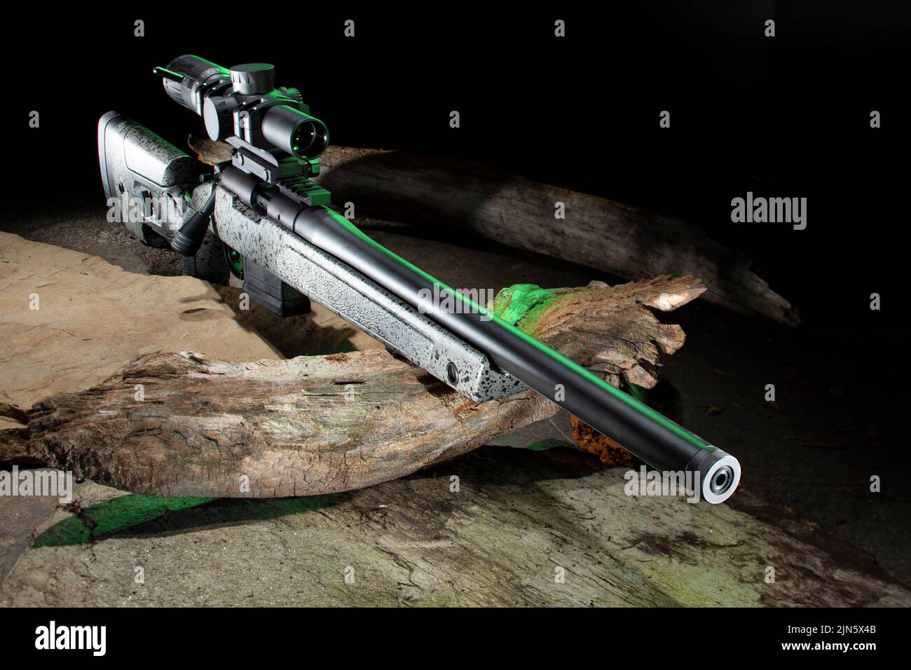 Bolt action rifle with a scope on wood and stones with green highlights Stock Photo