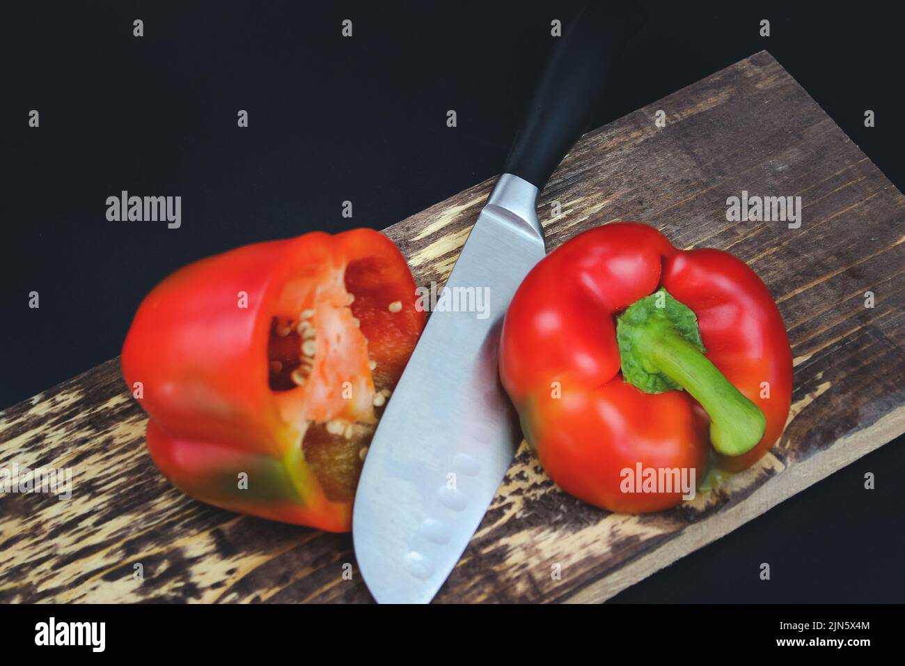 Knife cutting red pepper on wooden board. Stock Photo